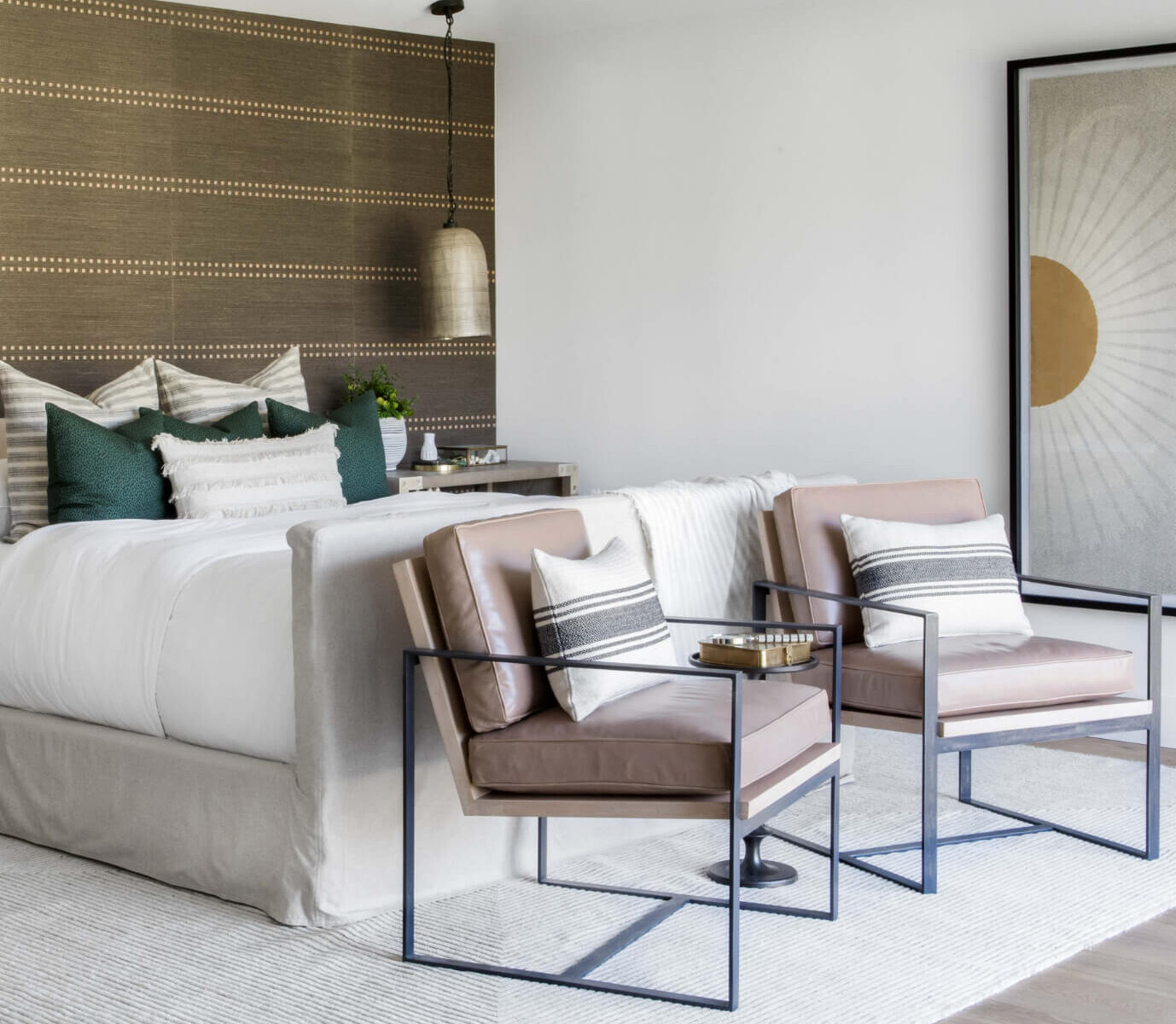 Luxury master bedroom featuring a spanish modern interior design with textured pillows on king sized bed and contemporary leather lounge chairs with a woven natural wallpaper