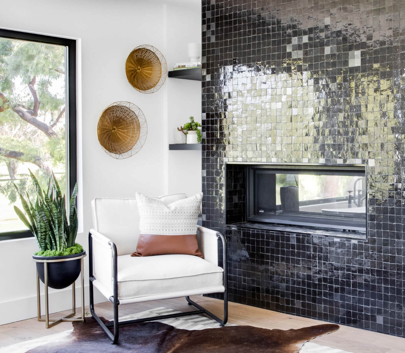 Spanish modern home interior design featuring a fireplace tiled with dark green ceramic tiles with white canvas lounge chair styled with a potted snake plant and cowhide rug